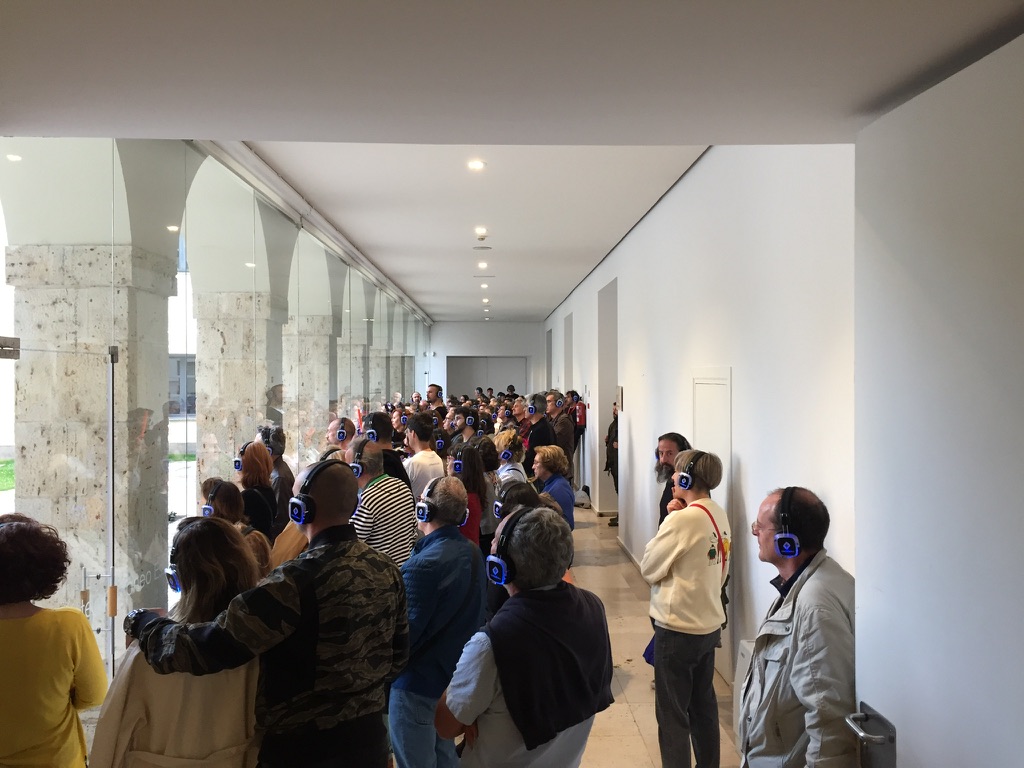 Publico con auriculares inalambricos de pie en una galeria del Museo Patio Herreriano