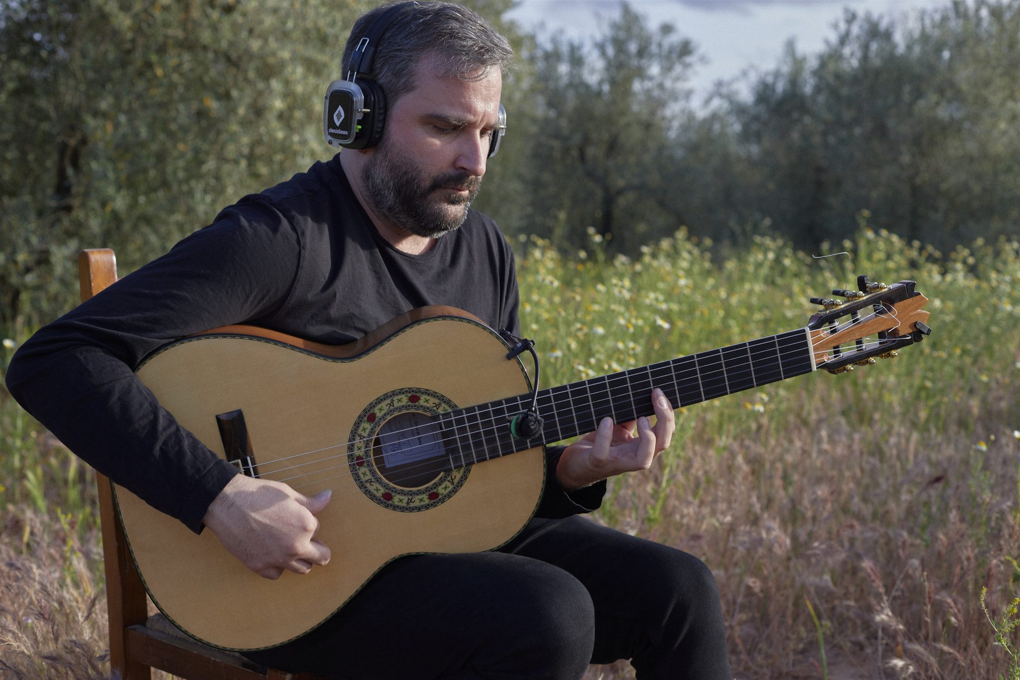 Eduardo Trassierra playing guitar with headphones in the olive grove at La Aceitera