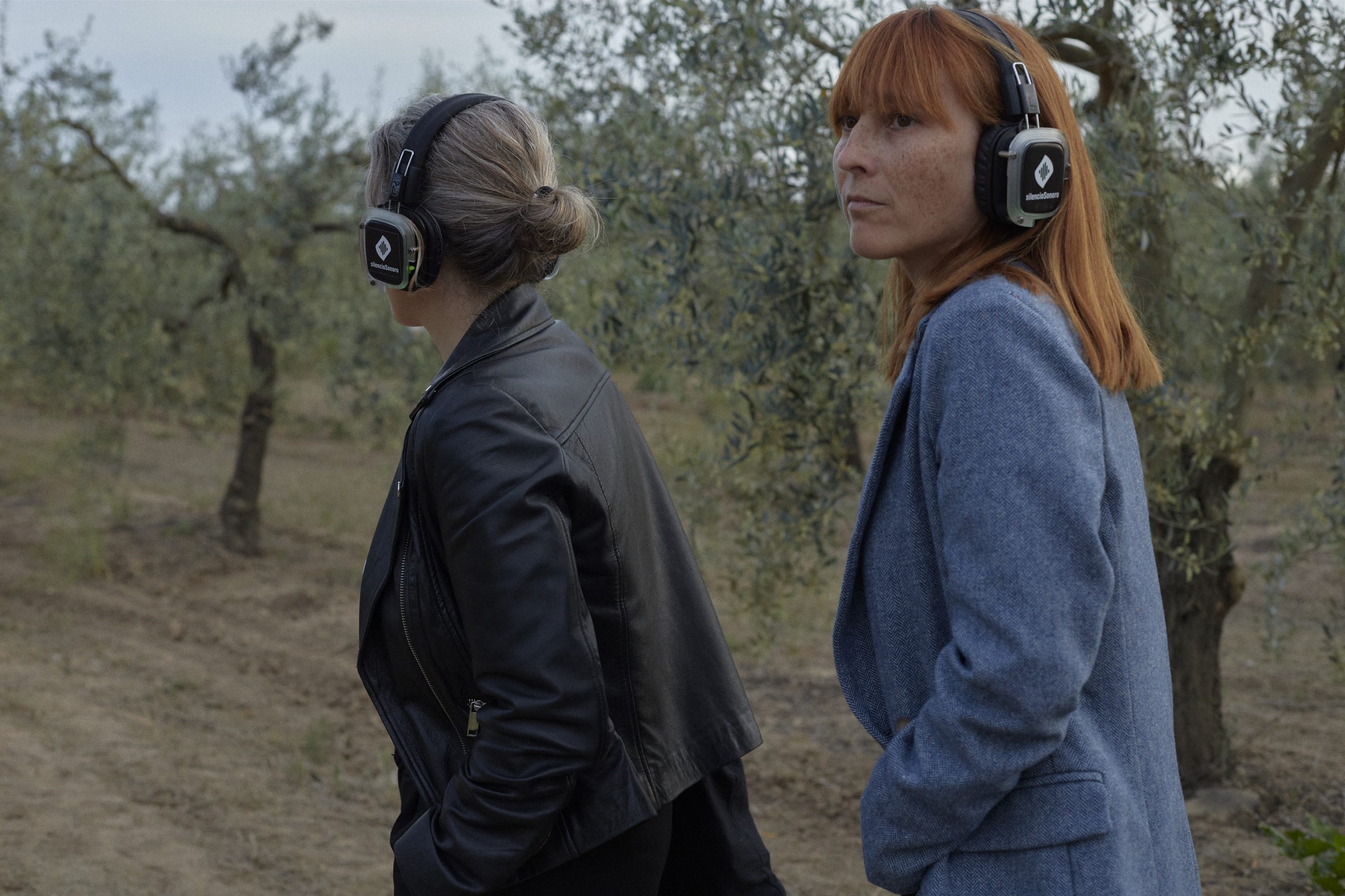 Dos asistentes con auriculares inalámbricos caminando entre los olivos